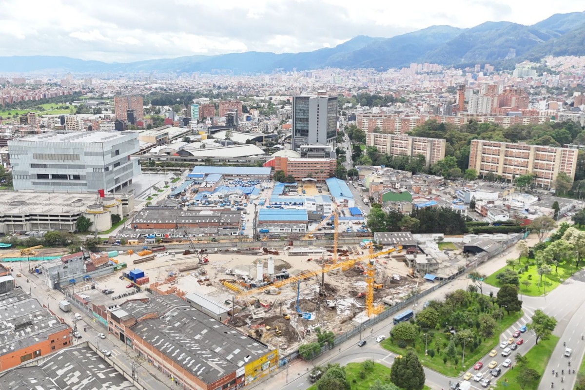 Vista aérea de una zona urbana con edificios, vías y un amplio proyecto de construcción con grúas, rodeado de árboles y montañas